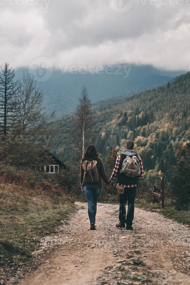 Long road. Full length rear view of young couple holding hands while hiking in mountains photo