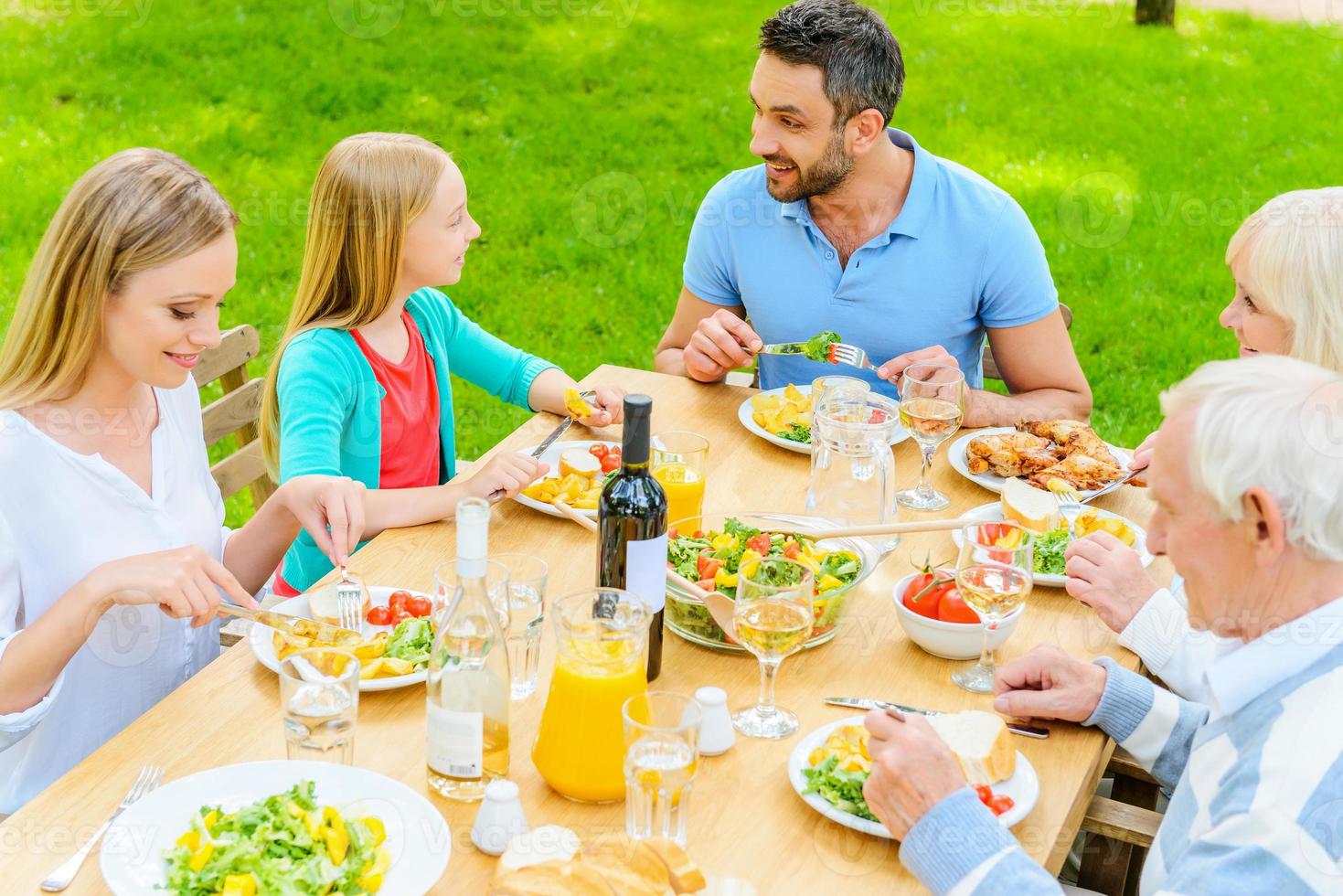 Enjoying dinner together. Top view of happy family of five people communicating and enjoying meal together while sitting at the dining table outdoors photo