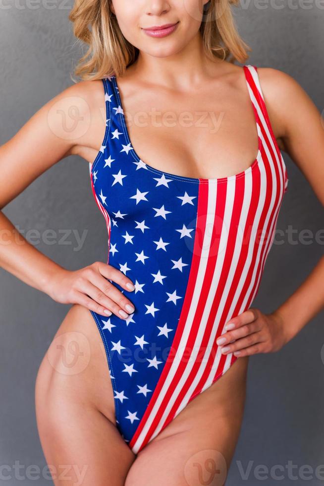 Proud of her perfect curves. Cropped image of attractive young blond hair woman in swimwear holding hands on hip while standing against grey background photo