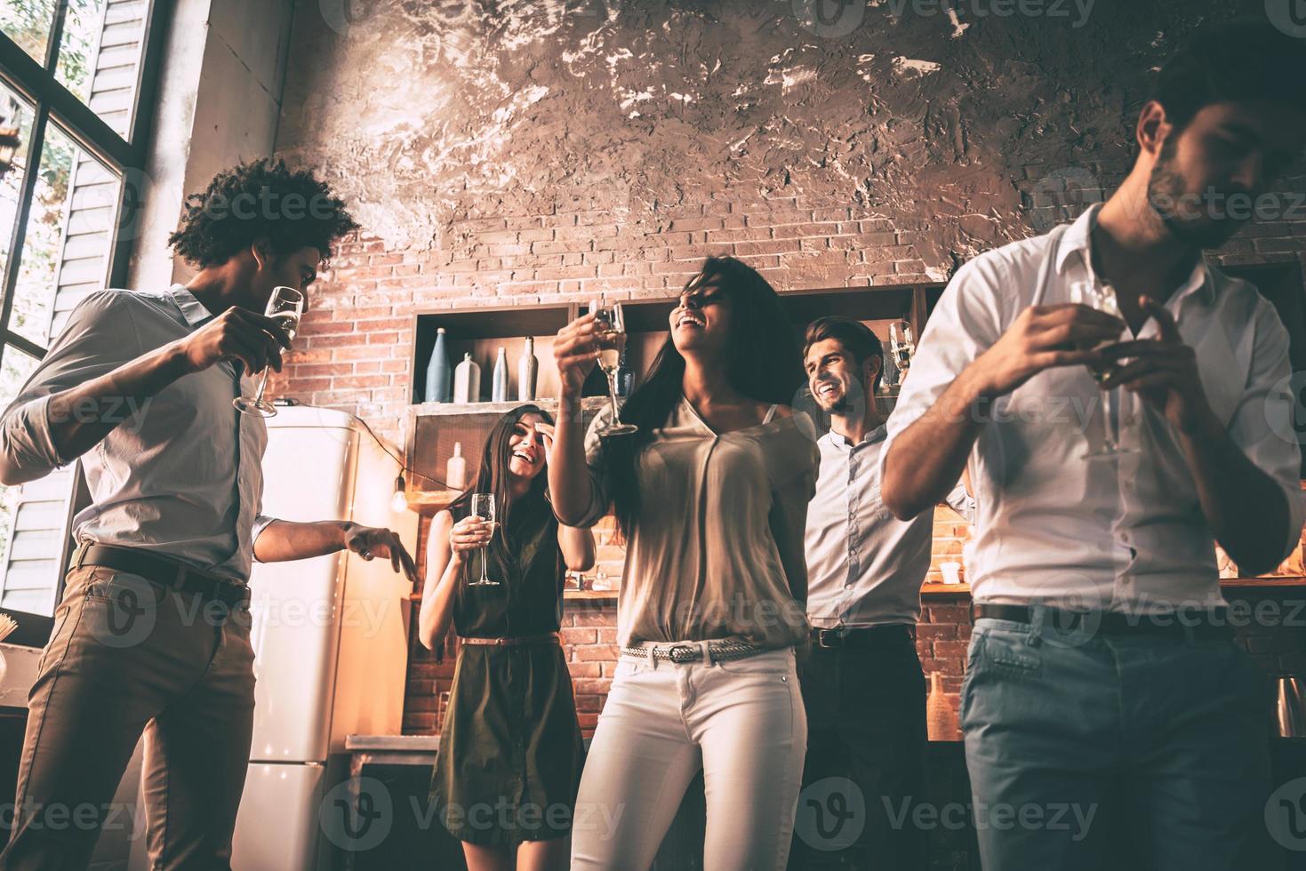 Just dance Low angle view of cheerful young people dancing and drinking while enjoying home party on the kitchen photo