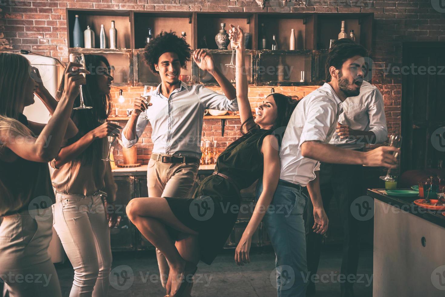 Having fun with friends. Cheerful young people dancing and drinking while enjoying home party on the kitchen photo