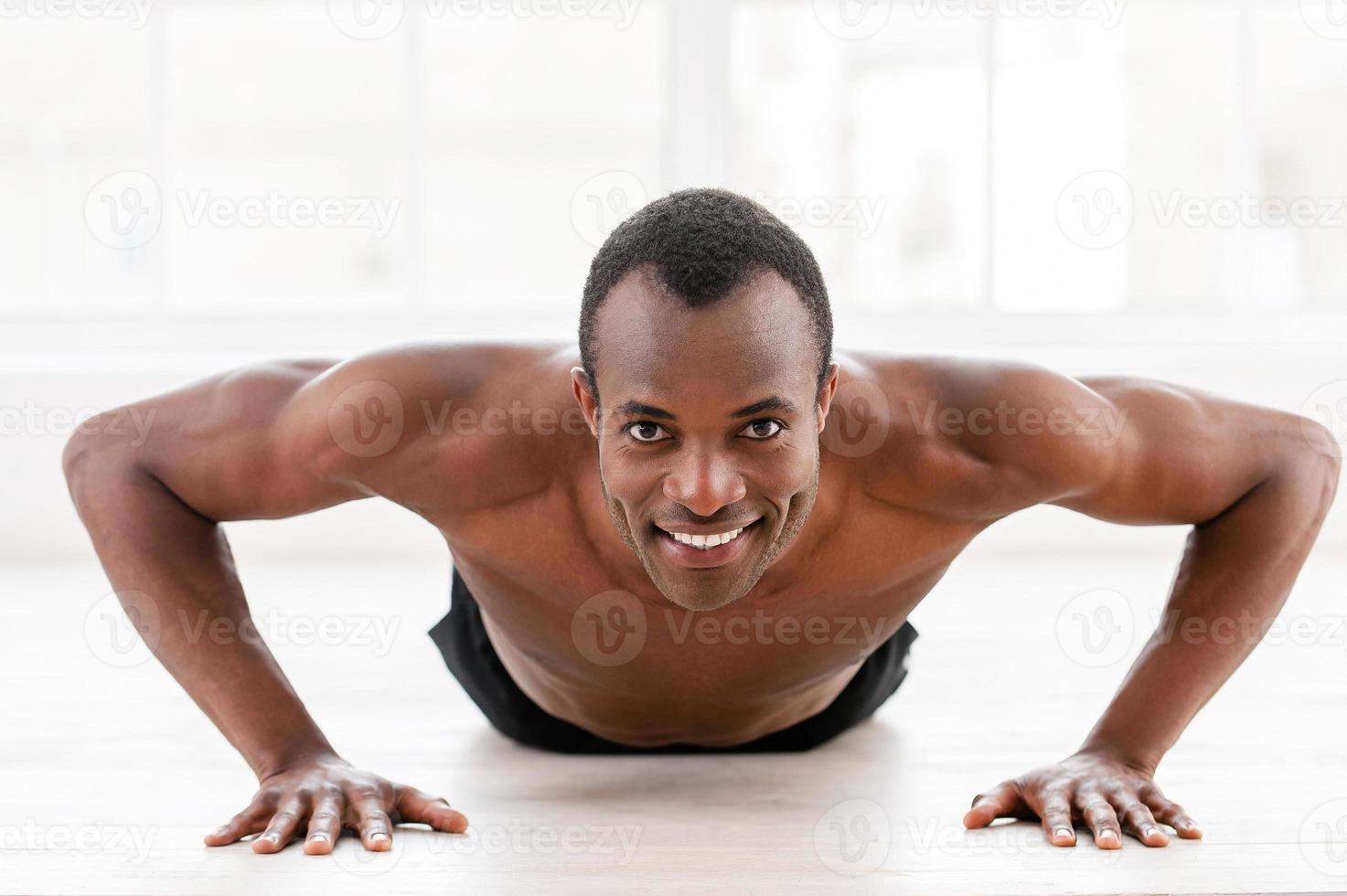 Man doing push-ups. Young muscular African man doing push-ups and looking at camera photo