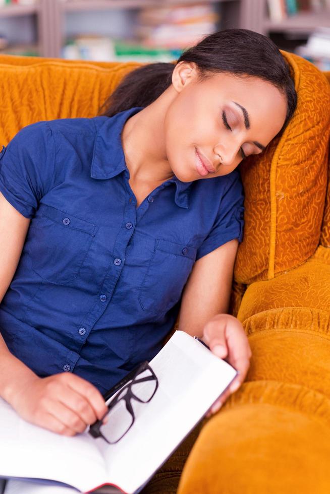 Tired student. Beautiful African female student sleeping in armchair while holding a book photo