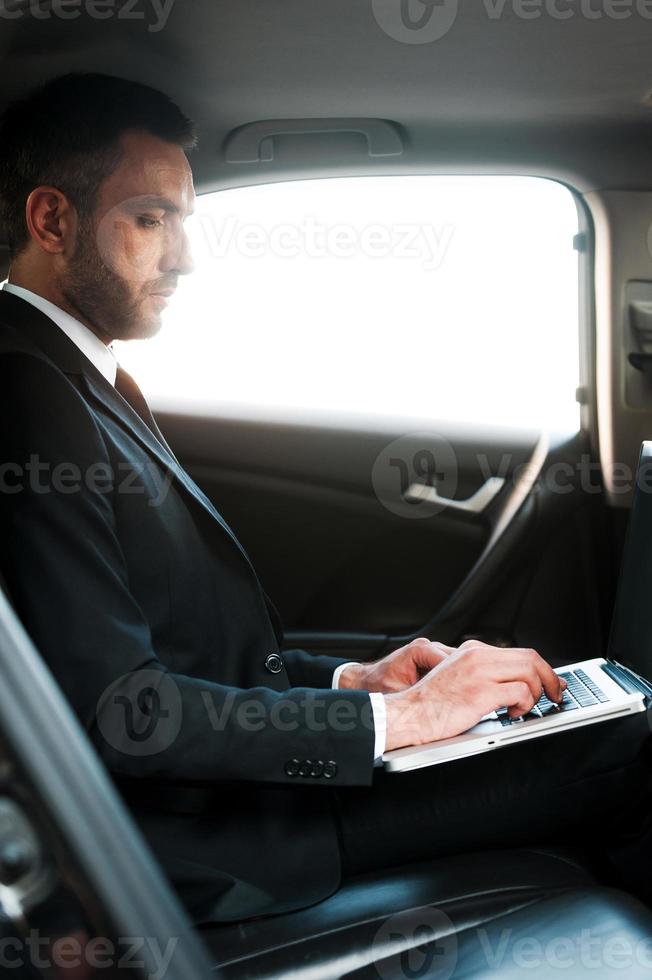 Businessman on the go. Confident young businessman working on laptop while sitting inside his car photo