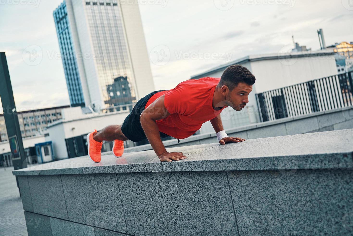 Strong young man in sports clothing keeping plank position while exercising outdoors photo