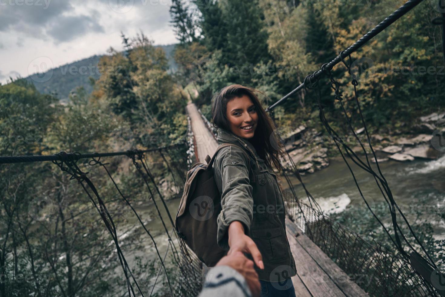 Beautiful young smiling woman holding hands with her boyfriend while walking on the suspension bridge photo