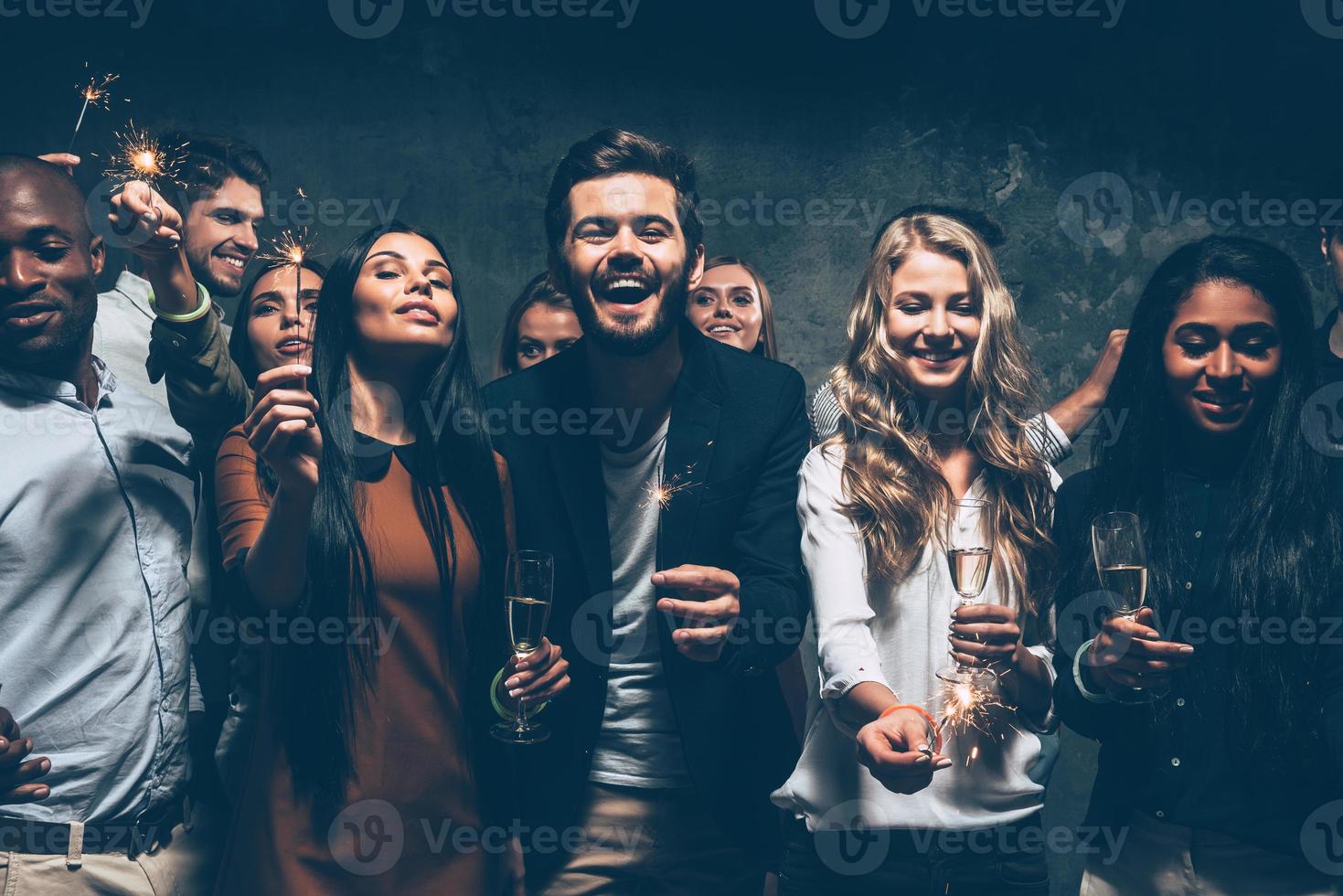 Celebrating with fun. Group of cheerful young people carrying sparklers and champagne flutes photo