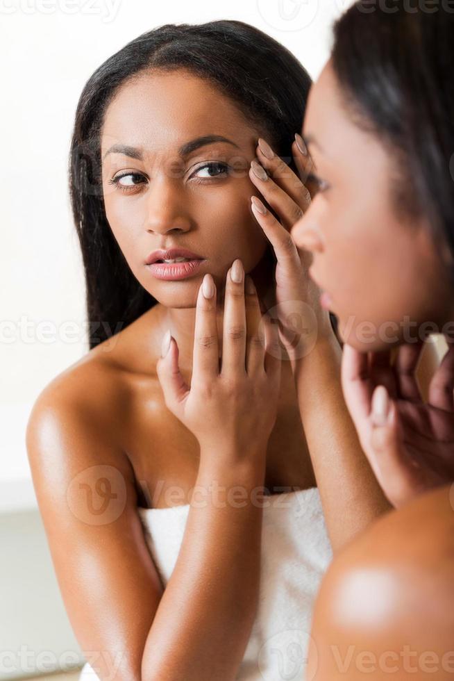 es acné concentrado joven africana tocándose la cara y mirándose en un espejo foto