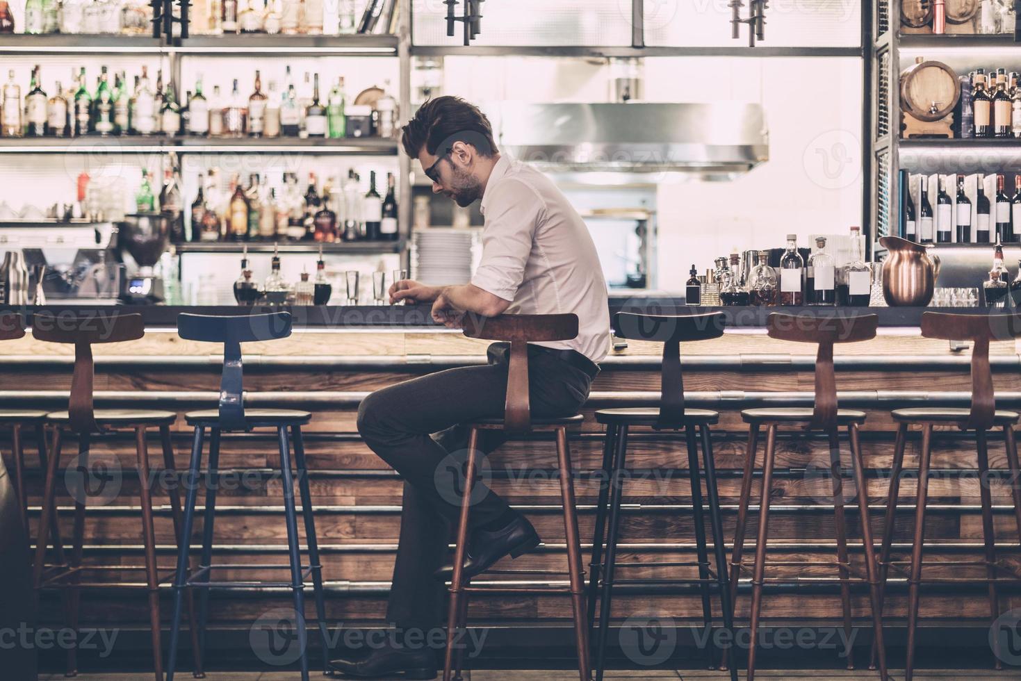 Tired businessman in bar. Frustrated young man in smart casual wear sitting at the bar counter photo