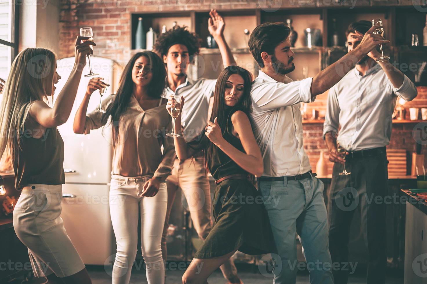 Party time Cheerful young people dancing and drinking while enjoying home party on the kitchen photo