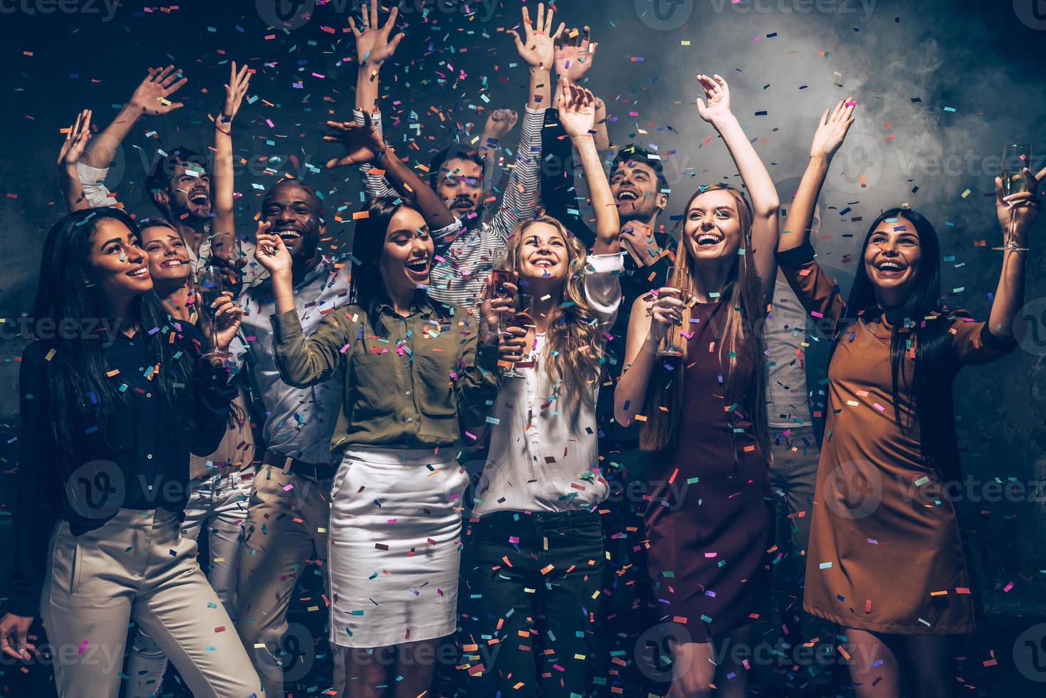 Perfect night. Group of beautiful young people throwing colorful confetti and looking happy photo