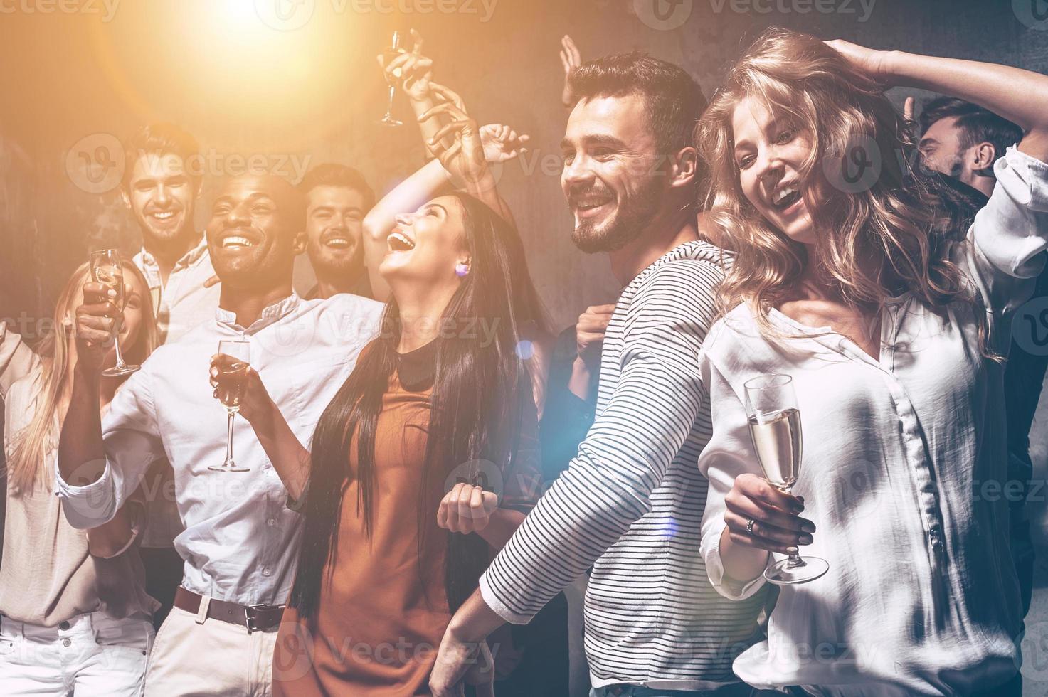 They love dancing. Group of beautiful young people dancing with champagne flutes and looking happy photo