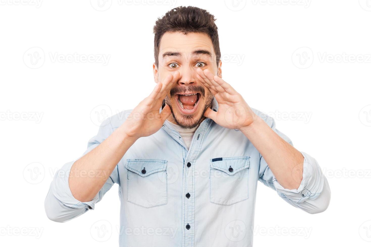 Great news Cheerful young man in holding hands near mouth and shouting while standing against white background photo