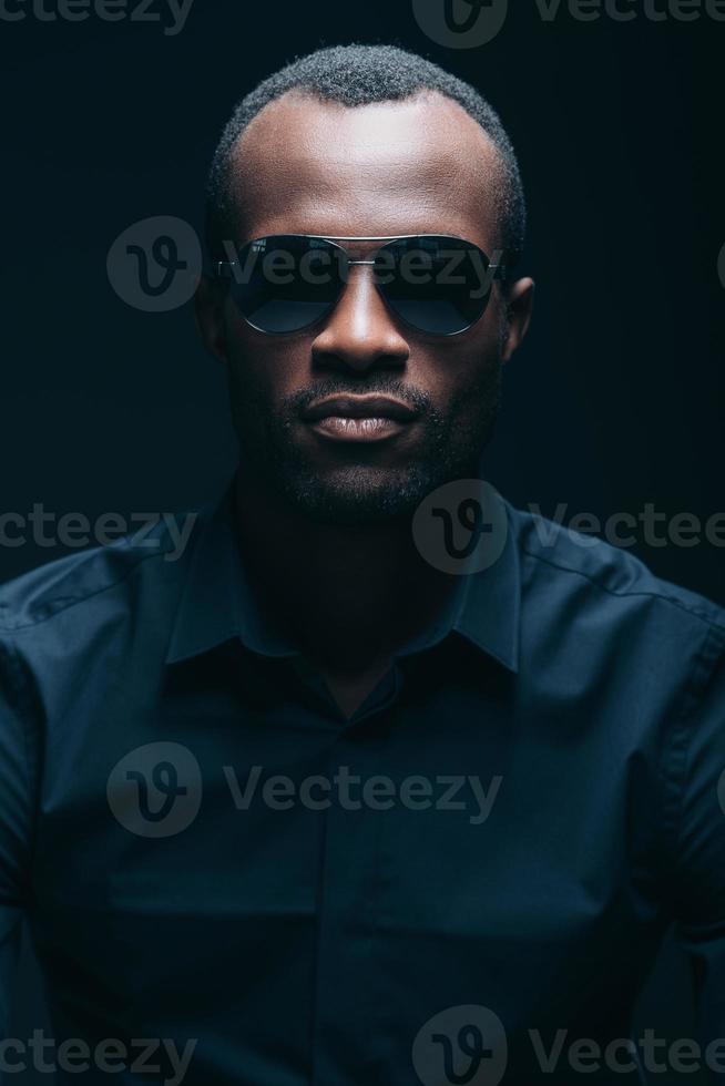 Cool and handsome. Portrait of handsome young African man in sunglasses looking at camera while being in front of black background photo