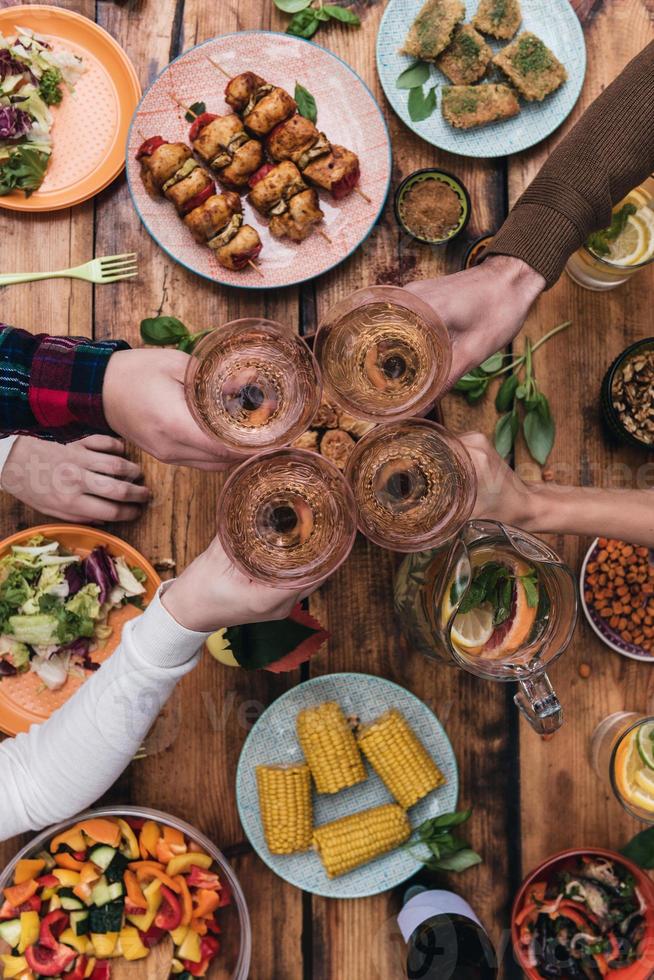 Cheers to friends Top view of four people cheering with wine while sitting at the rustic dining table photo