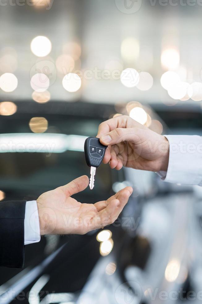 Here is your key Close up of man giving key to the car owner while standing in front of a car photo