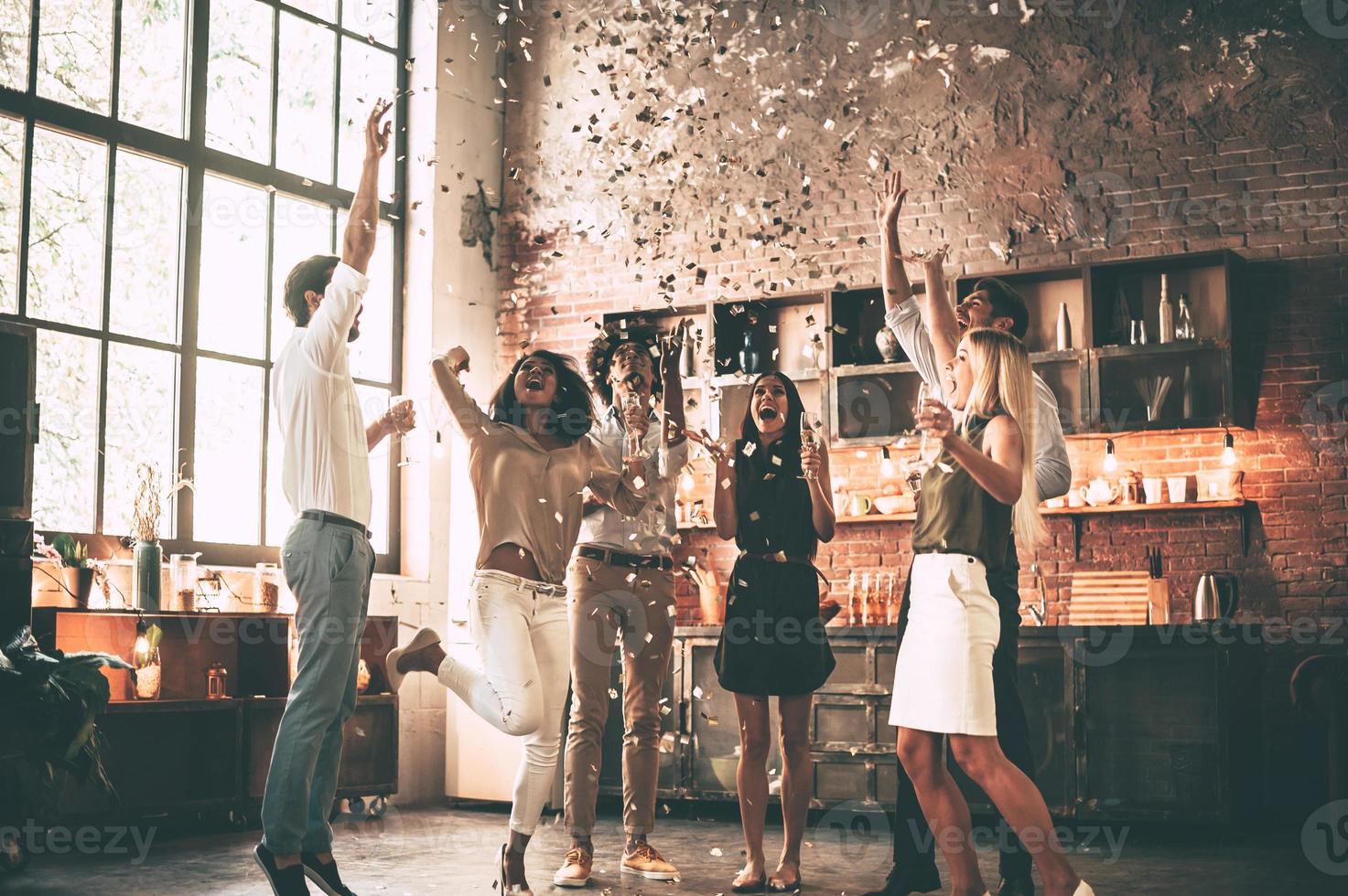 Simplemente pasándolo bien. toda la longitud de jóvenes alegres tirando confetti y saltando mientras disfrutan de una fiesta en casa en la cocina foto