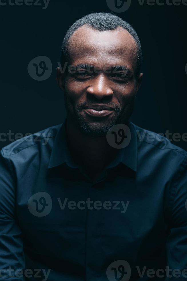 Always stay real Portrait of handsome young African man looking at camera with smile while being in front of black background photo