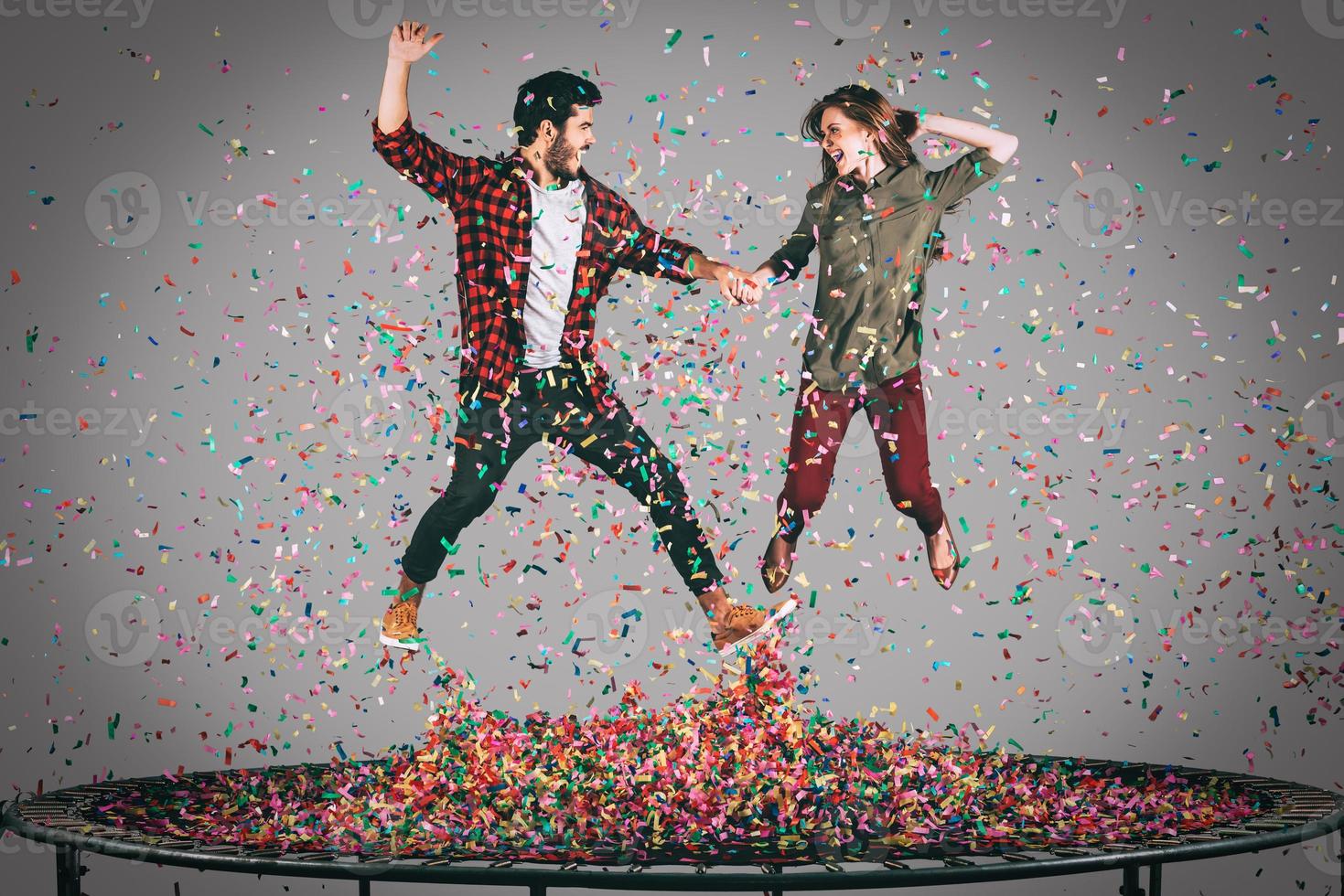 Trampoline fun. Mid-air shot of beautiful young cheerful couple holding hands while jumping on trampoline together with confetti all around them photo