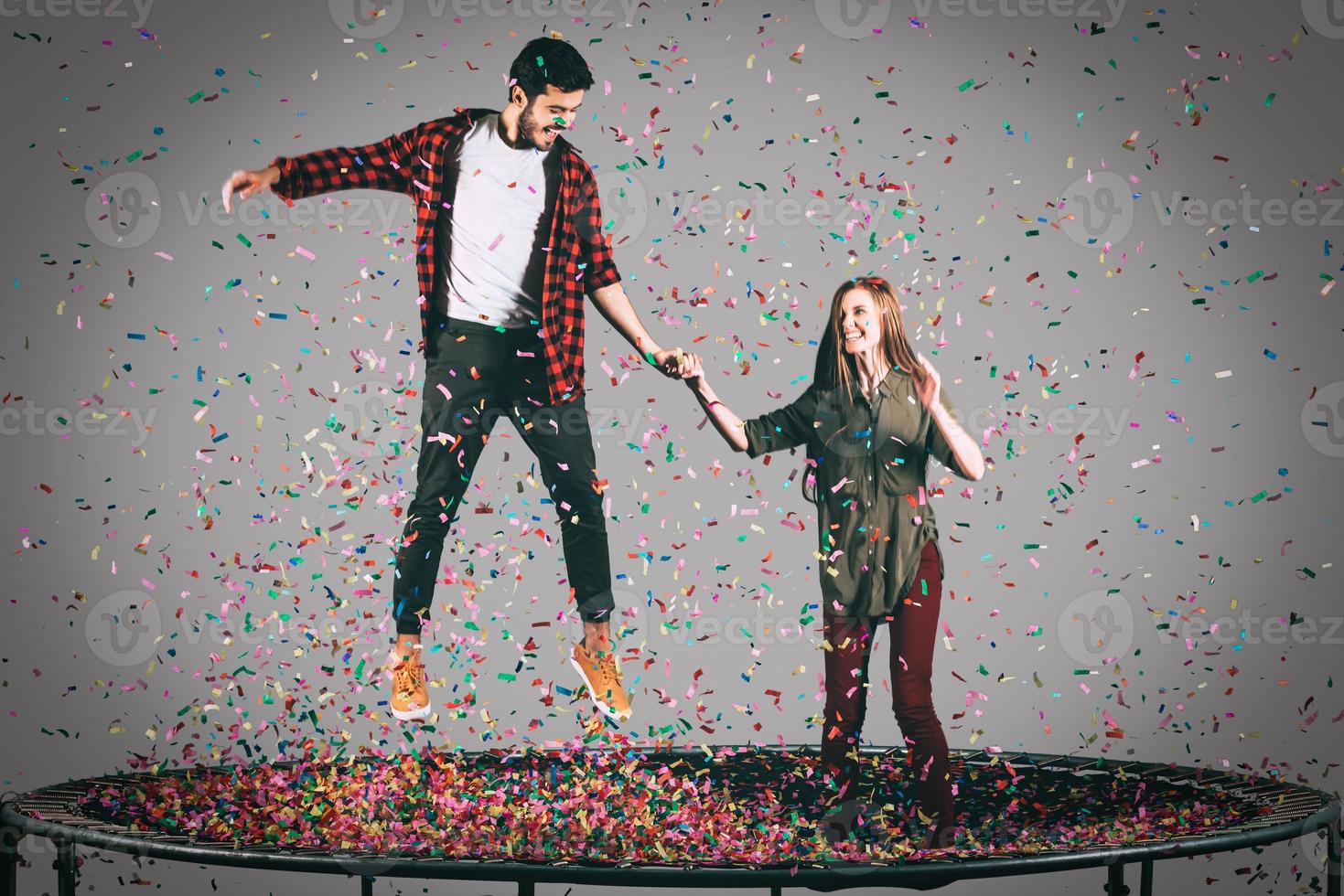 tiempo de diversión toma en el aire de una hermosa pareja joven y alegre saltando en un trampolín junto con confetti a su alrededor foto