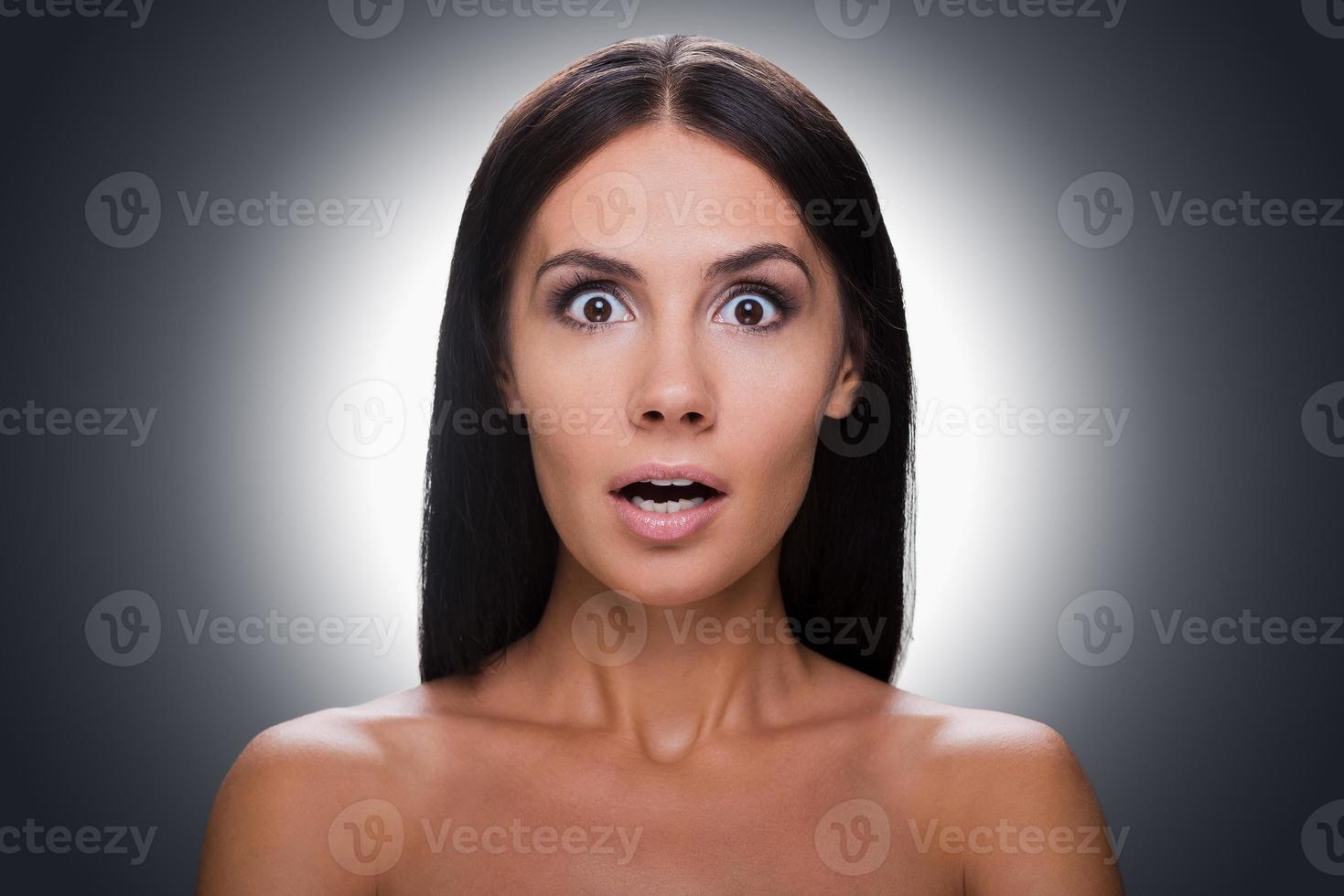 No way Portrait of surprised young shirtless woman looking at camera and keeping mouth open while standing against grey background photo
