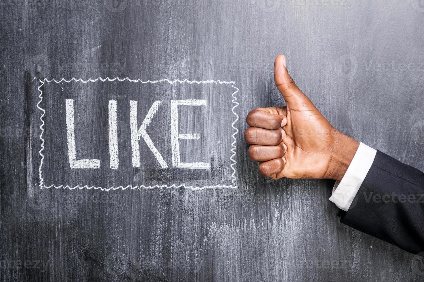 Like this Close-up of human hand with thumb up in front of the blackboard with inscription Like photo