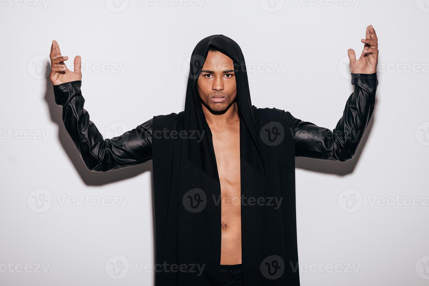 Power inside. Confident young African man in hooded shirt looking at camera and keeping arms raised while standing against white background photo