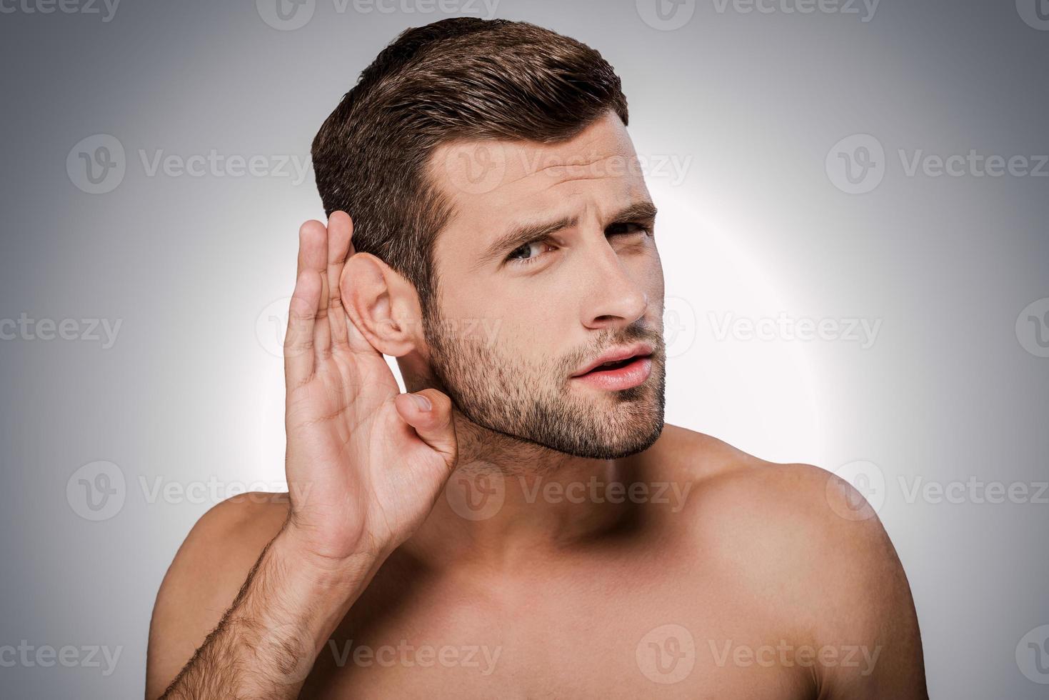 What did you say Portrait of handsome young shirtless man eavesdropping while standing against grey background photo