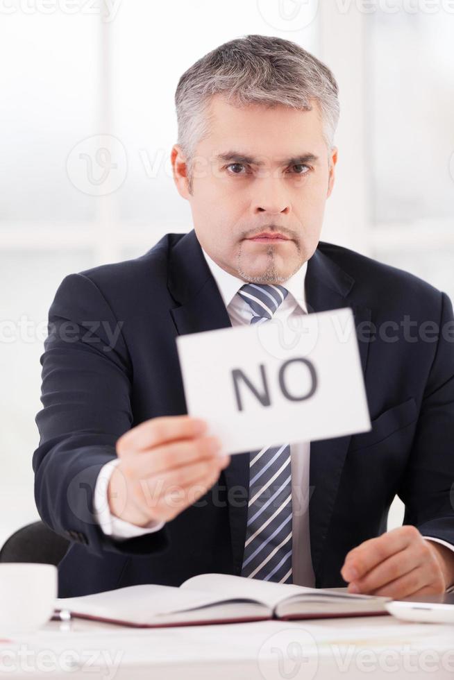 I said no Serious senior man in formalwear holding a paper with no sign on it while sitting at her working place photo