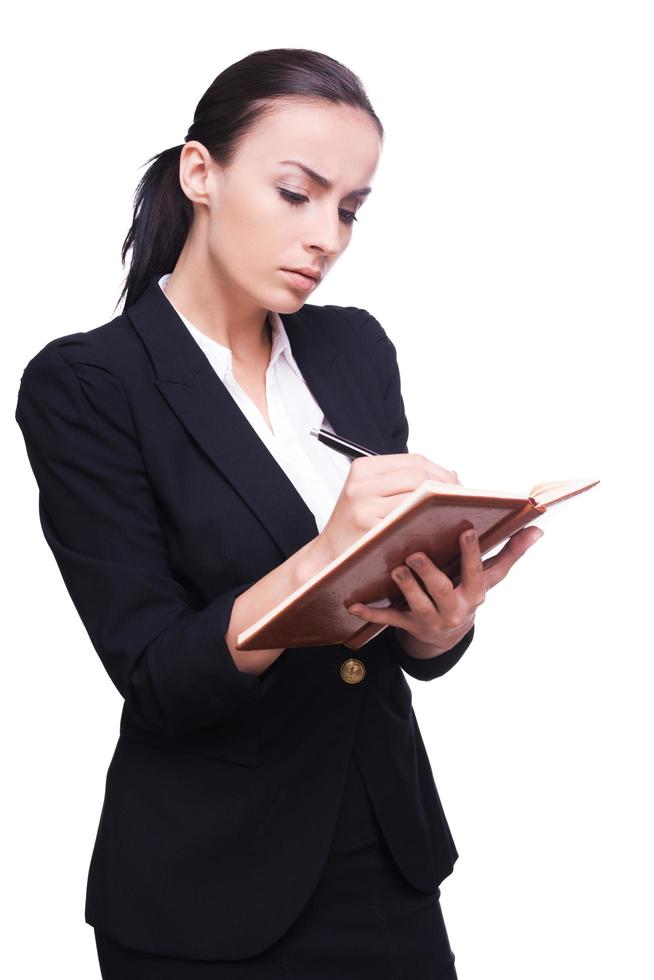 Writing down her ideas. Confident young businesswoman writing something in her note pad while standing isolated on white photo