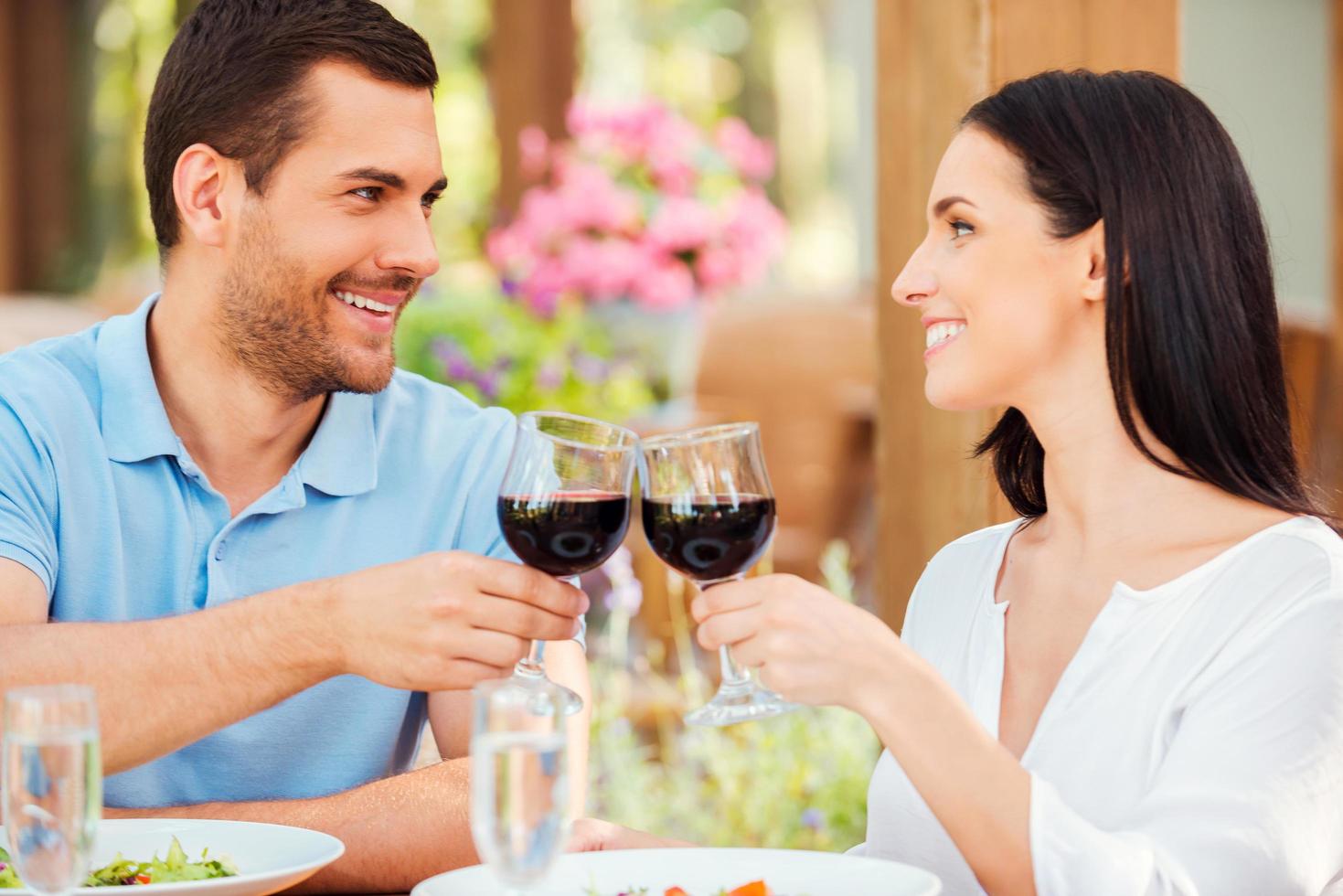 Romantic date in restaurant. Happy young loving couple toasting with red wine and smiling while relaxing in outdoors restaurant together photo