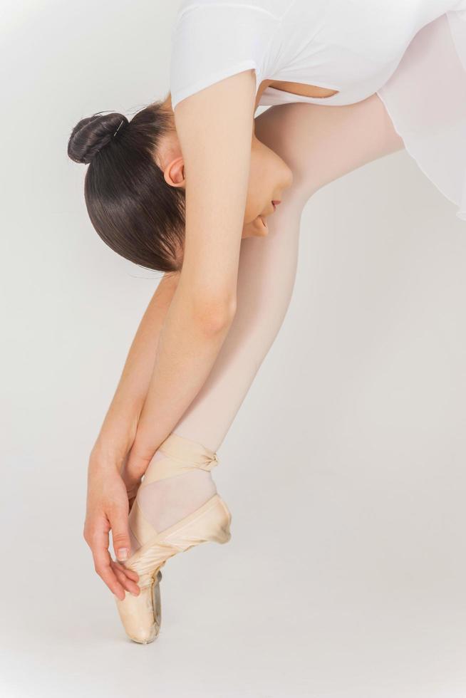 Stretching routine. Close-up of young ballerina doing stretching exercises while standing against white background photo