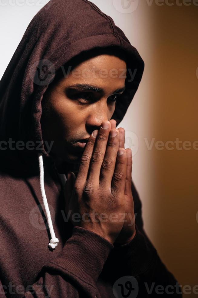 Full concentration. Confident young African man in hooded shirt keeping hands clasped near face and looking away photo