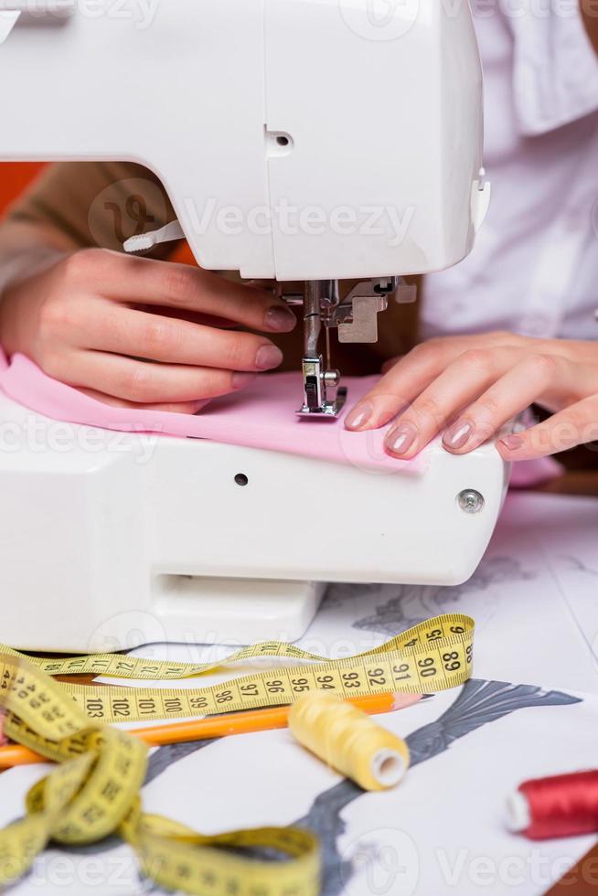 Working on sewing machine. Close-up of female fashion designer working on sewing machine while sitting at her working place photo