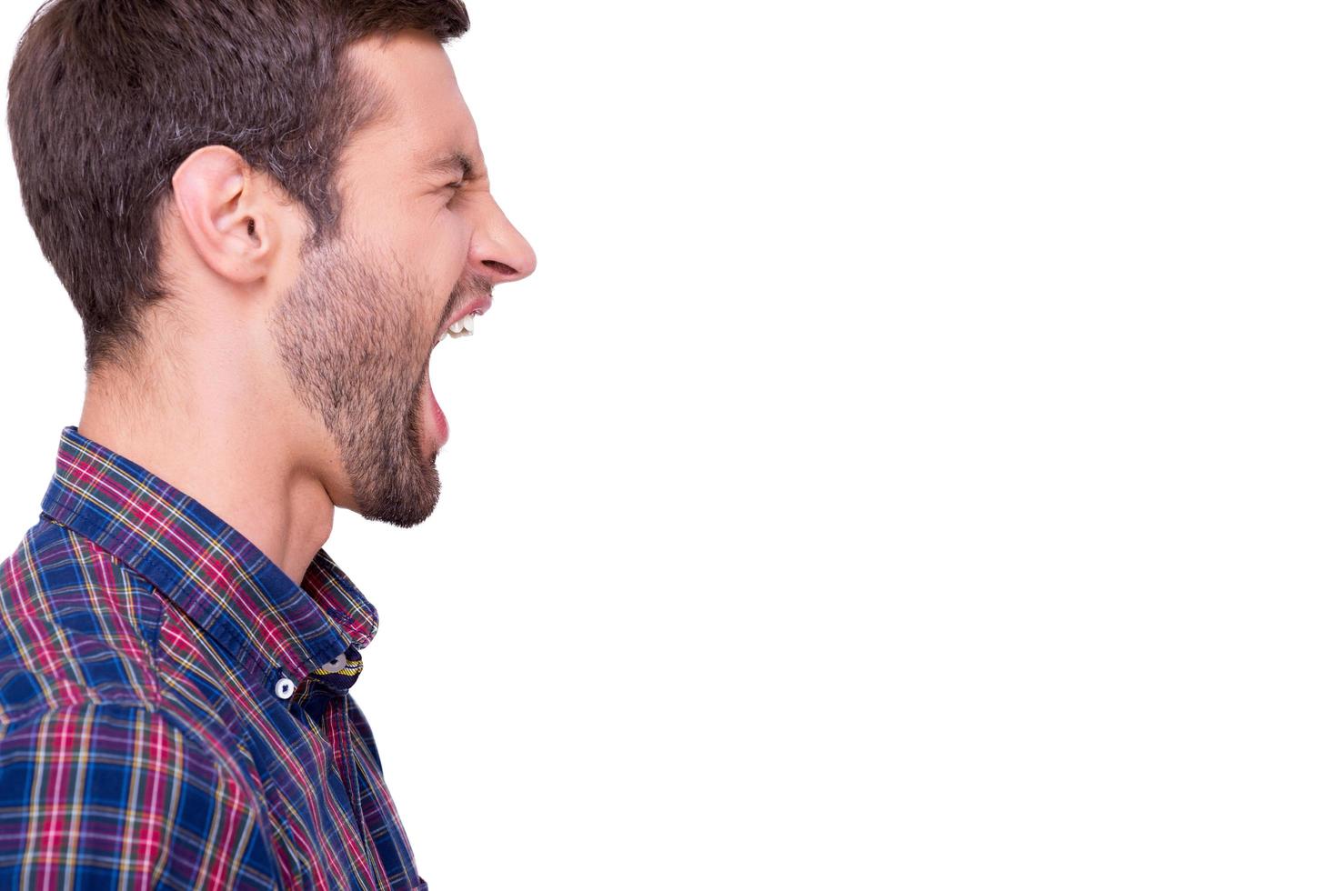 Shouting out loud. Side view of furious young man shouting and keeping eyes closed  while standing isolated on white photo