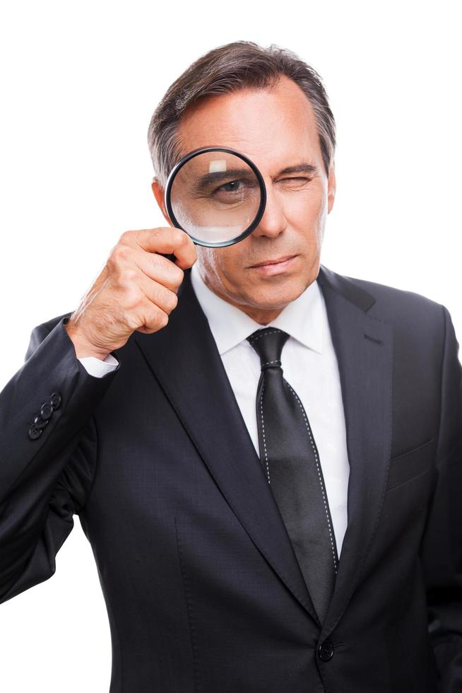 Businessman examining you. Serious mature man in formalwear examining you with magnifying glass while standing isolated on white background photo