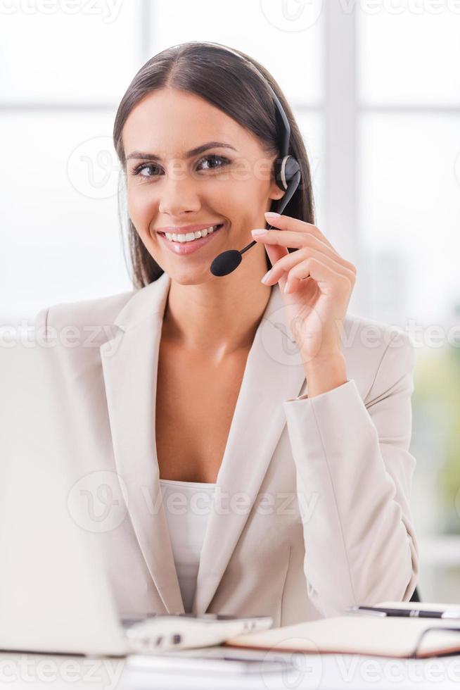 Supporting your business. Beautiful young businesswoman adjusting her headset and smiling while sitting at her working place photo