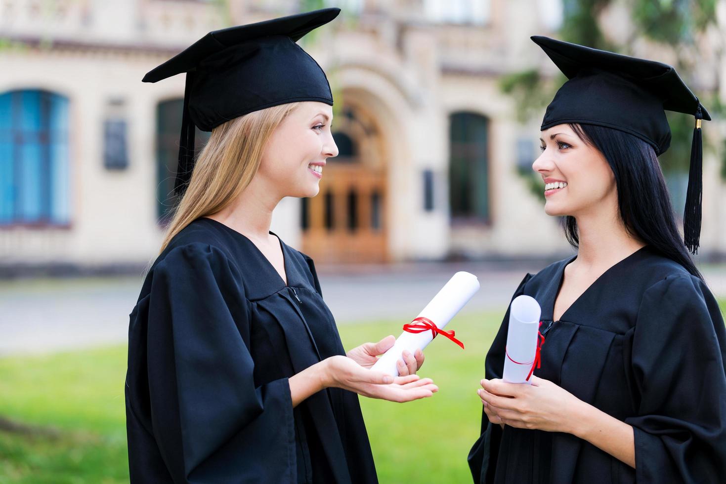 discutiendo la ceremonia. dos mujeres jóvenes felices en vestidos de graduación con diplomas y hablando foto