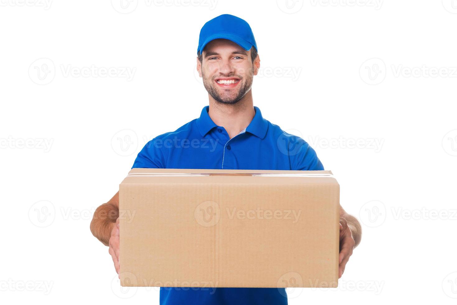tome su paquete feliz joven mensajero estirando una caja de cartón y sonriendo mientras está de pie contra el fondo blanco foto