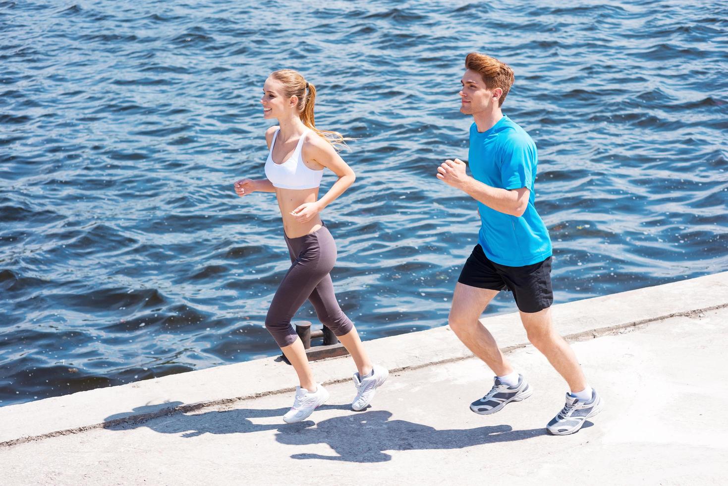 Jogging together.  Top view of young woman and man in sports clothing running along the riverbank photo