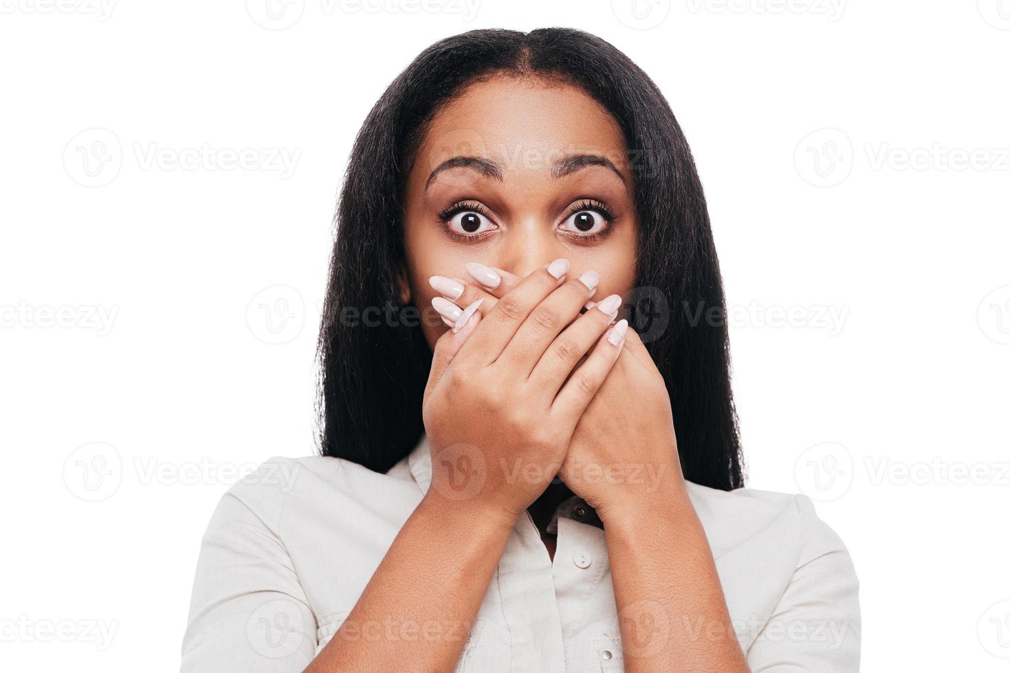Unbelievable news Shocked young African woman covering mouth with hands and looking at camera while standing against white background photo