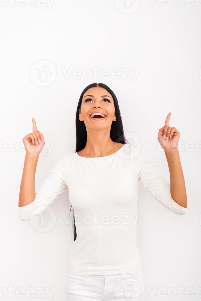 Look over there Cheerful young woman pointing up while standing against white background photo