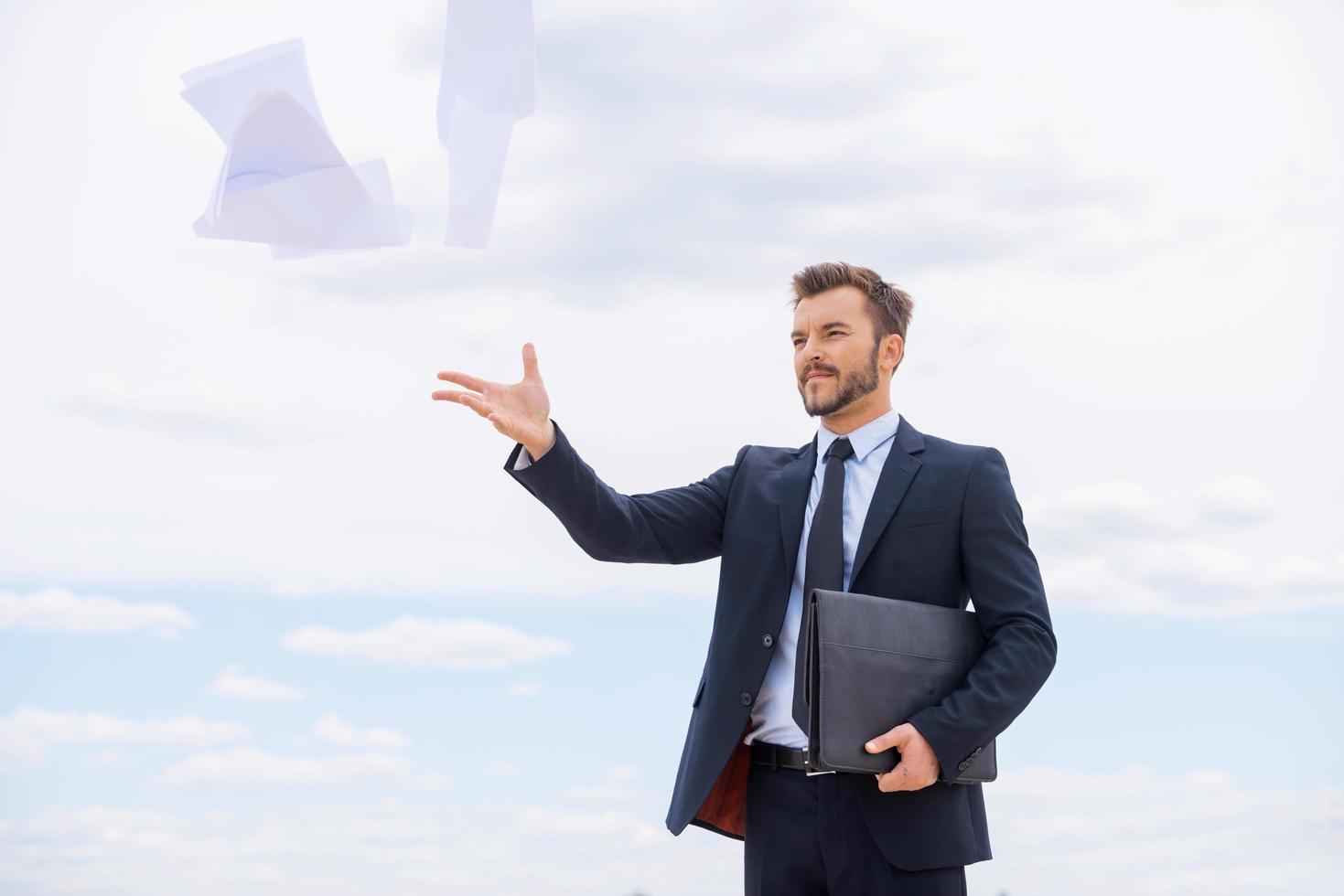 Tired of paperwork. Frustrated young businessman throwing documents away while standing against blue sky photo