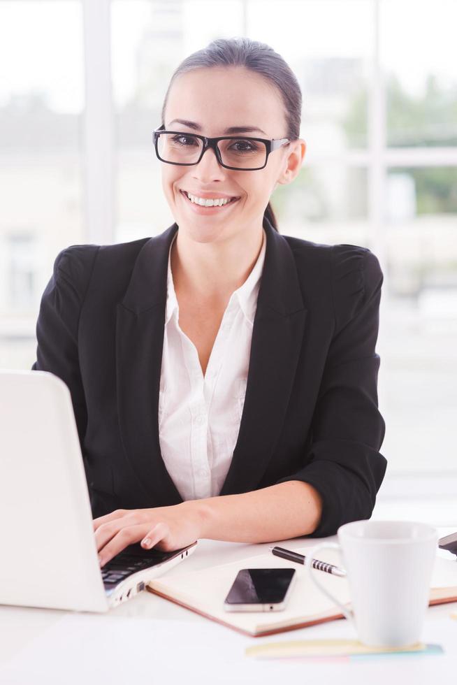 empresaria en el trabajo. mujer de negocios joven que usa la computadora y sonríe mientras está sentada en su lugar de trabajo foto