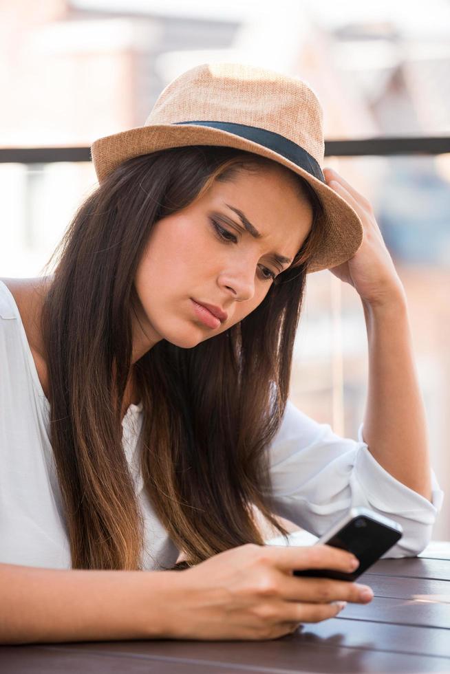 malas noticias. mujer joven deprimida con sombrero funky mirando el teléfono móvil mientras se sienta al aire libre foto