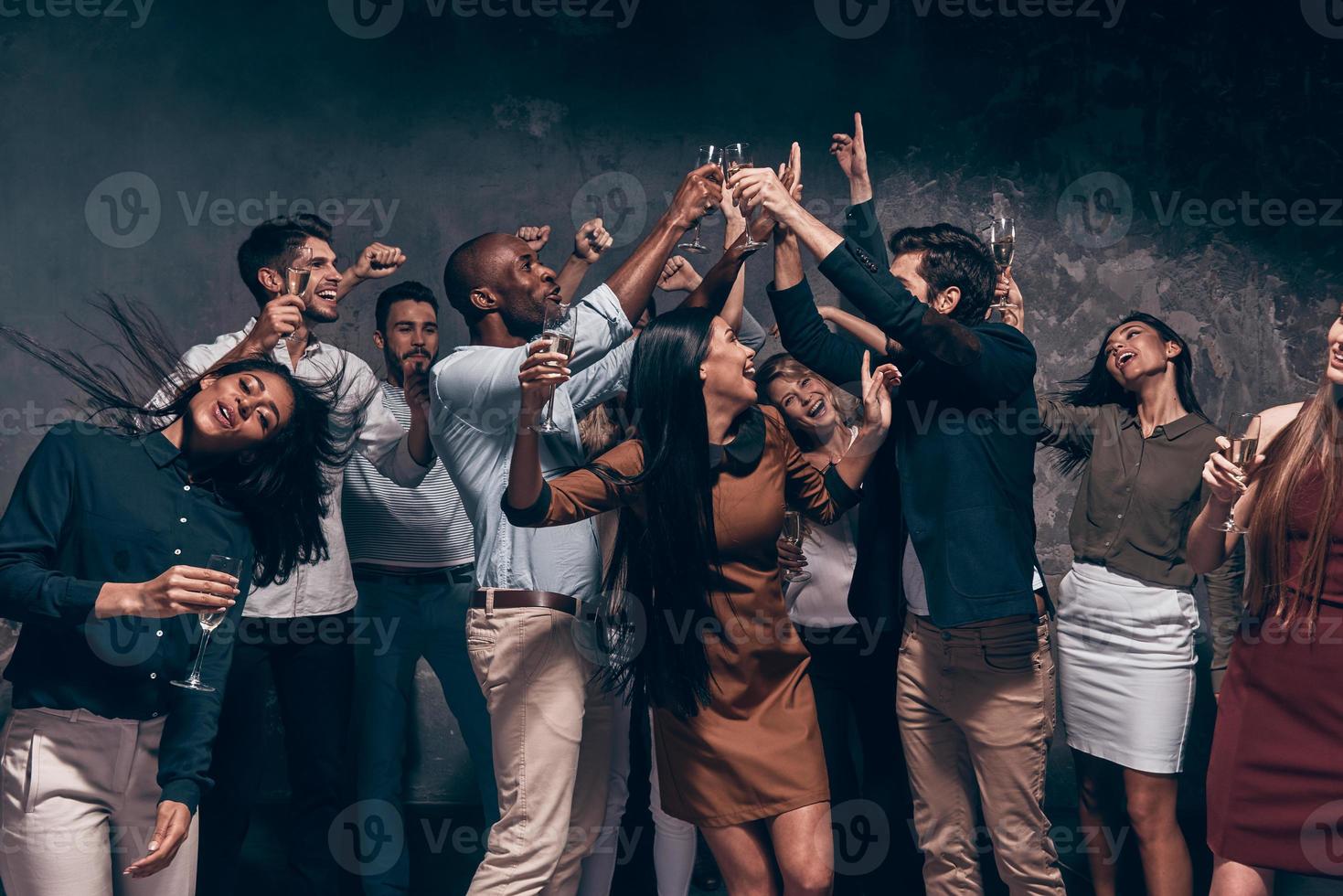 disfrutando de una fiesta increíble. grupo de hermosos jóvenes bailando con flautas de champán y luciendo felices foto