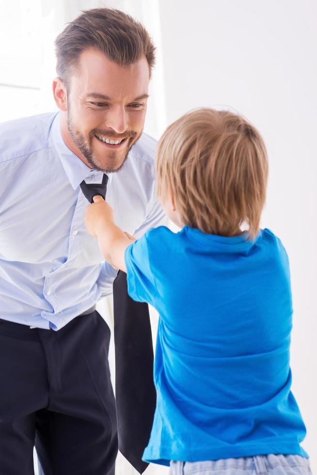 Making sure his father looks good. Playful little boy helping father to tie a necktie photo