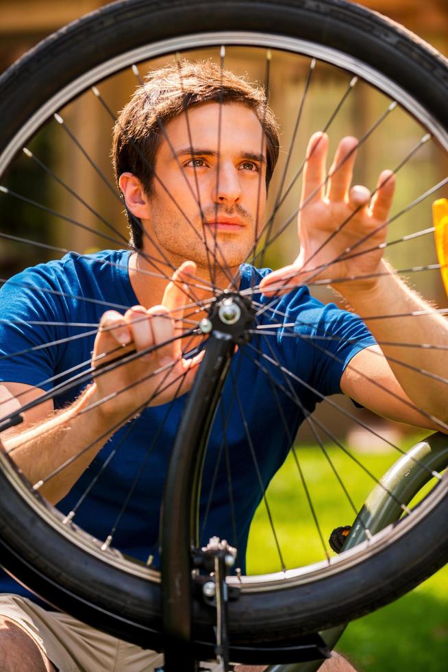 Sé cómo arreglarlo. un joven confiado arreglando su bicicleta mientras está de pie al aire libre foto