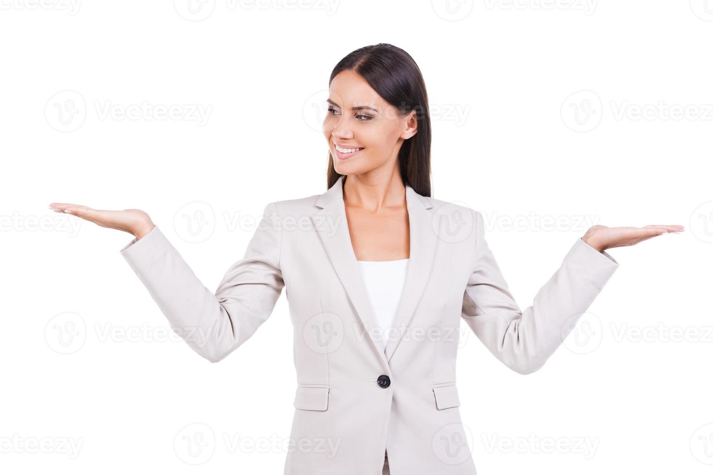 Hard choice. Beautiful young businesswoman in suit holding copy spaces in both hands and smiling while standing against white background photo