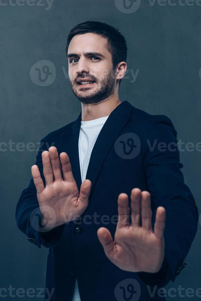 No way Frustrated young man looking at camera and gesturing while standing against grey background photo